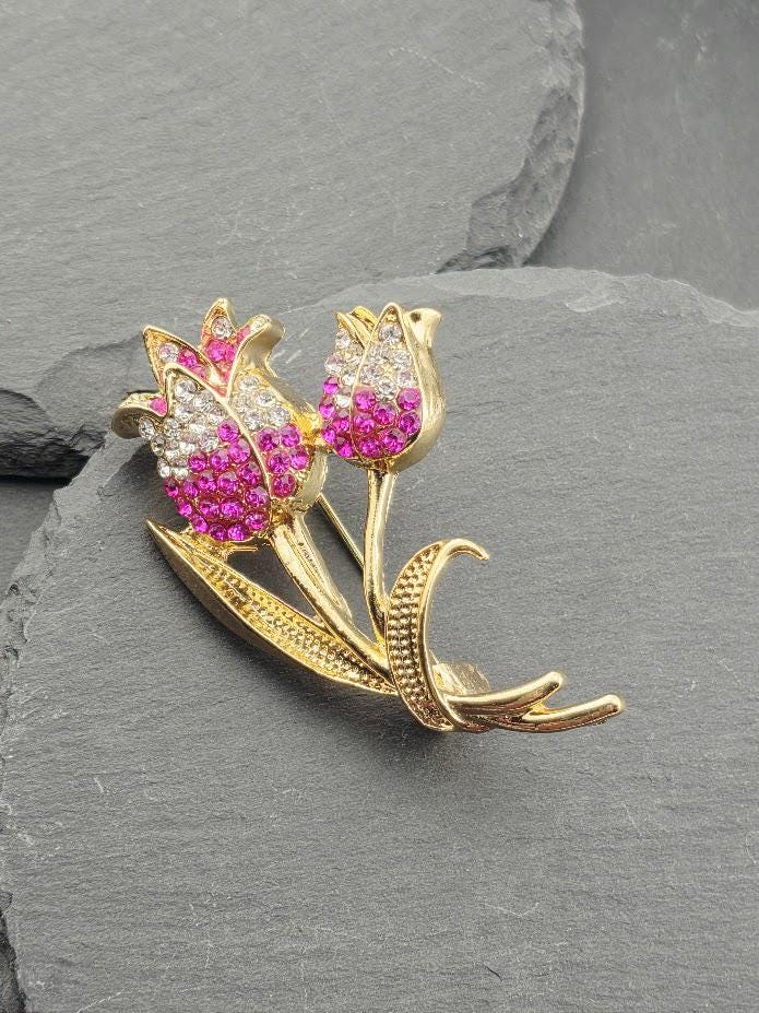 A decorative brooch with a floral design, featuring two pink flowers with sparkling gemstones.