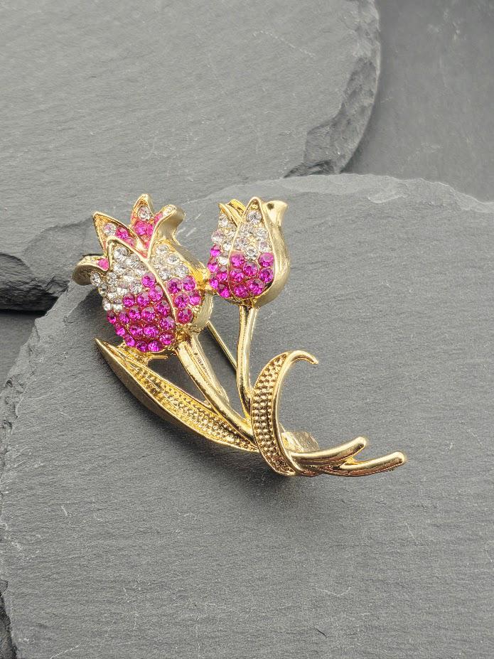 A decorative brooch with a floral design, featuring two pink flowers with sparkling gemstones.