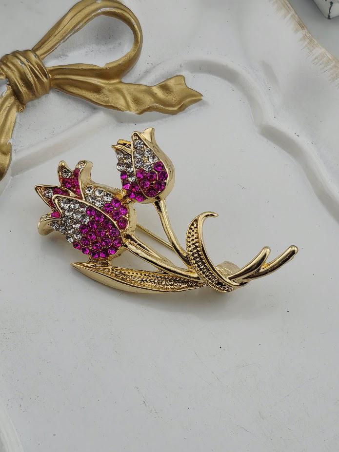 A decorative brooch with a floral design, featuring two pink flowers with purple gemstones.