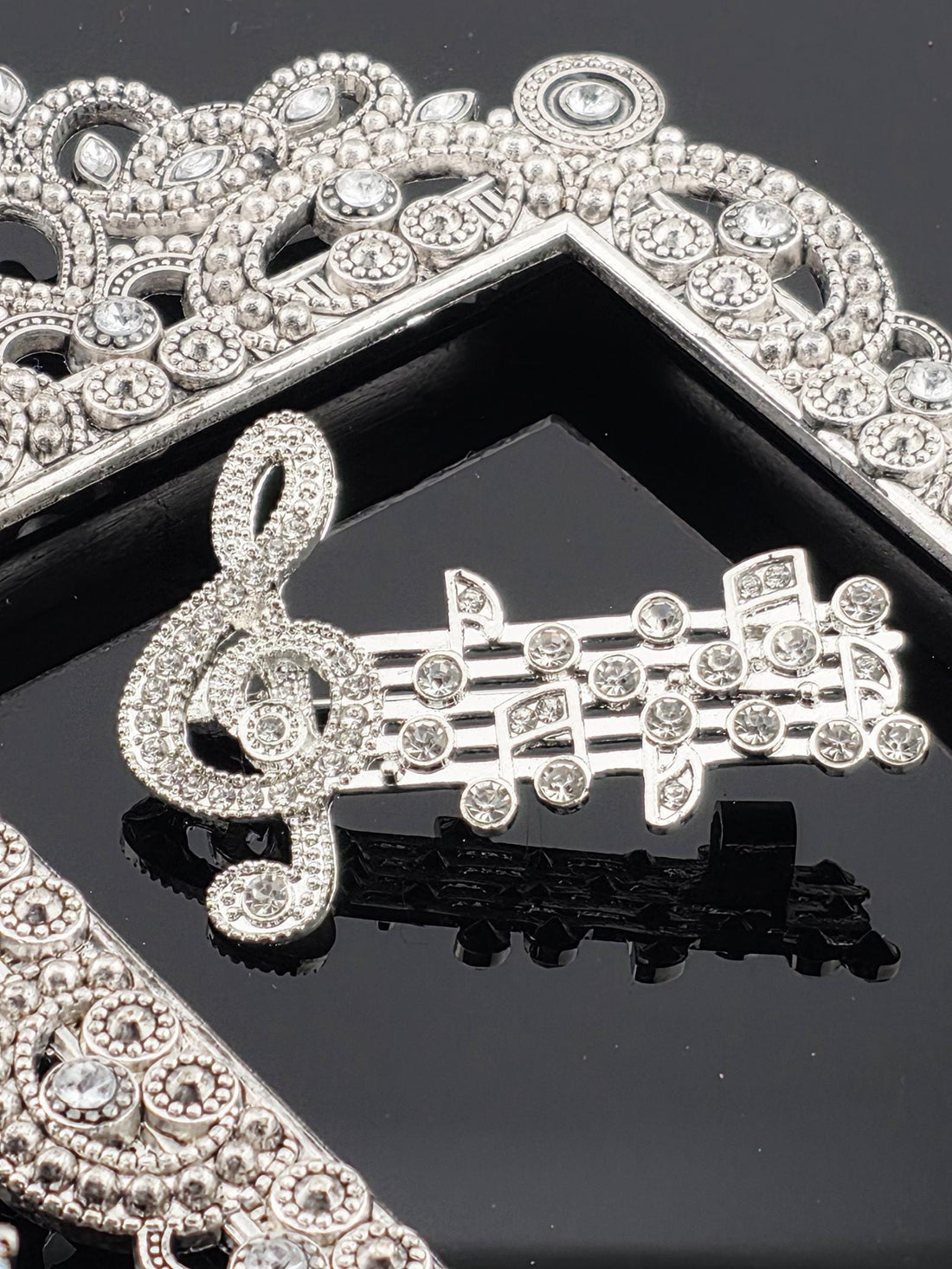 a close-up view of a piece of jewelry, possibly a necklace or bracelet, adorned with numerous sparkling diamonds. The jewelry appears to be a decorative piece, possibly a brooch or pendant, with intricate designs and patterns. The background is dark, which contrasts with the sparkling diamonds and highlights the details of the jewelry.