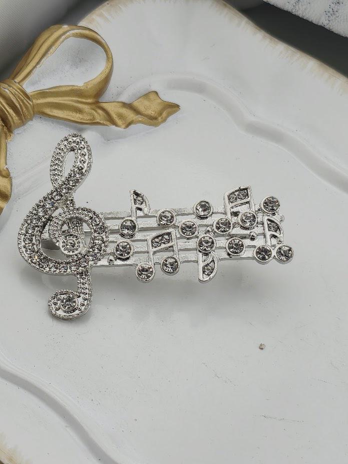 A silver brooch with a musical note design and sparkling rhinestones is displayed on a white surface.