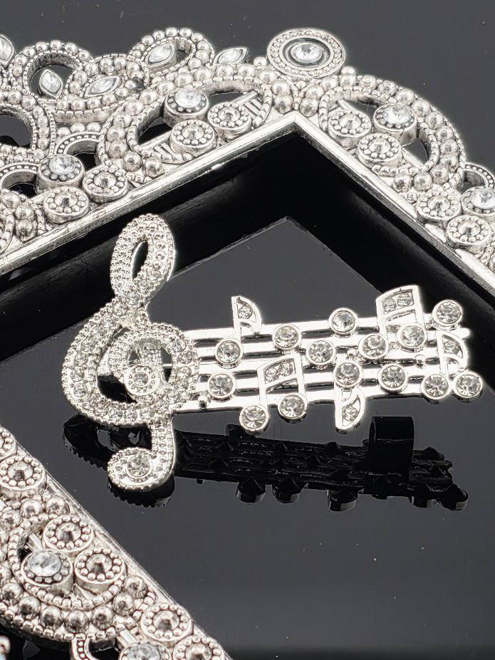 a collection of ornate, sparkling jewelry pieces, including a large silver brooch with a musical note design and a diamond-encrusted tiara.