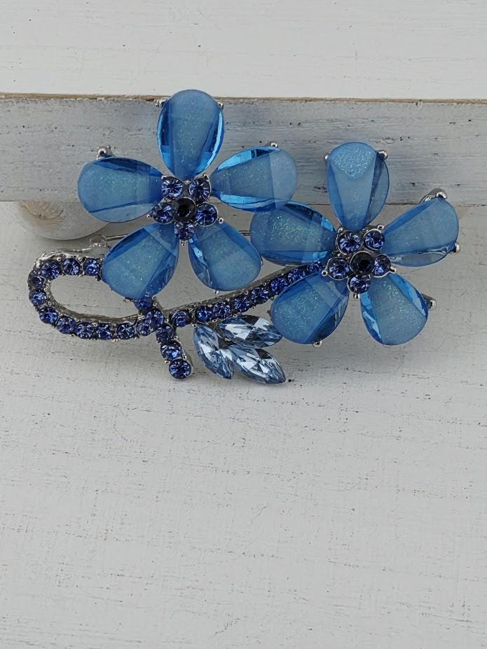 A decorative brooch with blue glass flowers and blue gemstones.