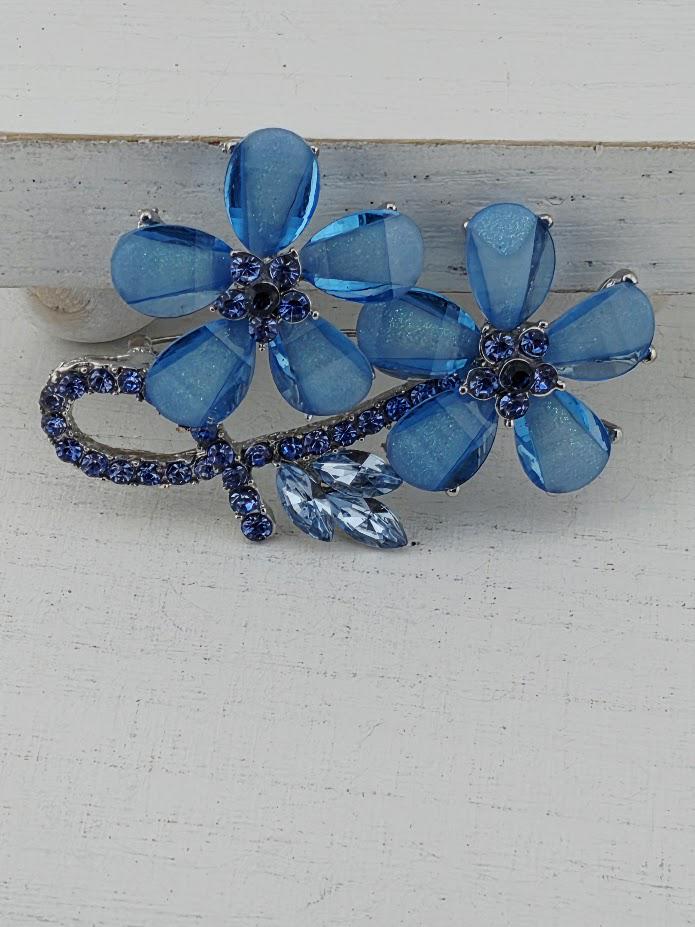 A decorative brooch with blue glass flowers and blue gemstones.