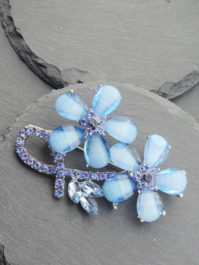 A decorative brooch with blue and clear gemstones, featuring a floral design with blue and clear gemstones.