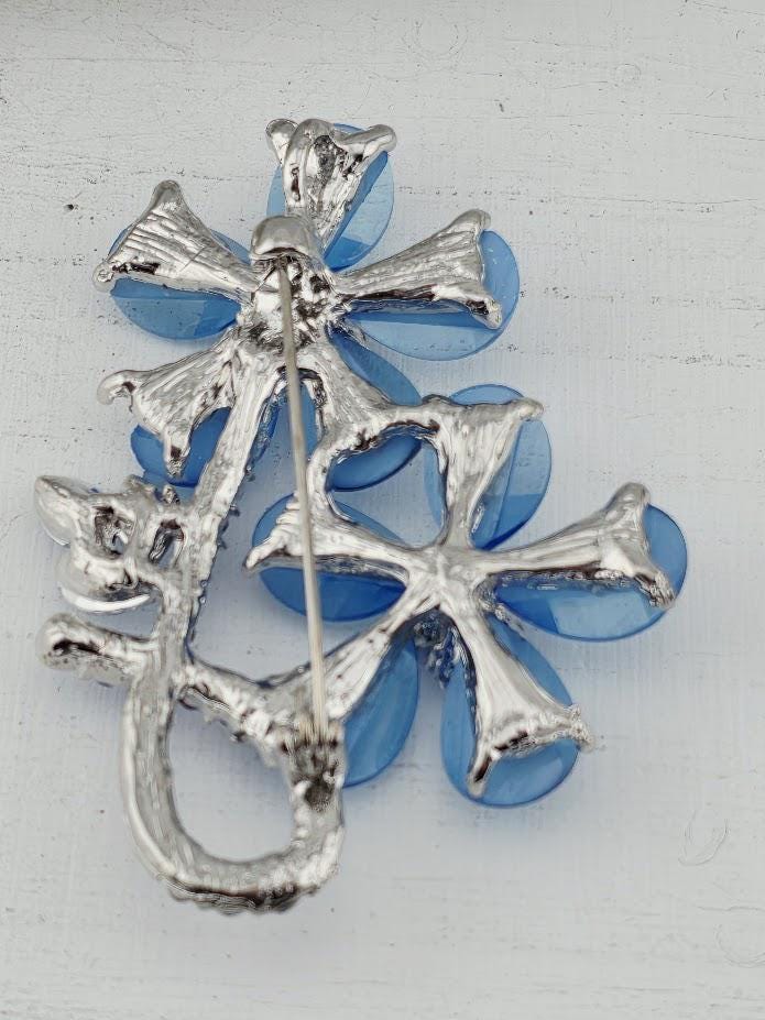 A silver pin with a flower-shaped design made of blue glass pieces.