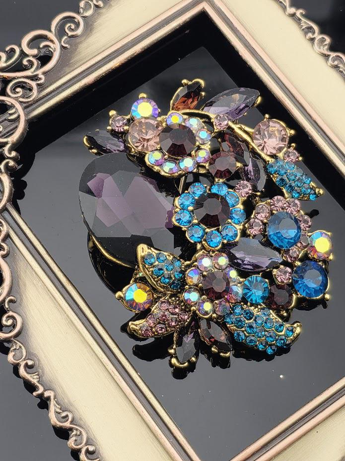 a decorative brooch with a variety of colorful gemstones and intricate designs, including purple, blue, and pink stones, as well as floral elements.