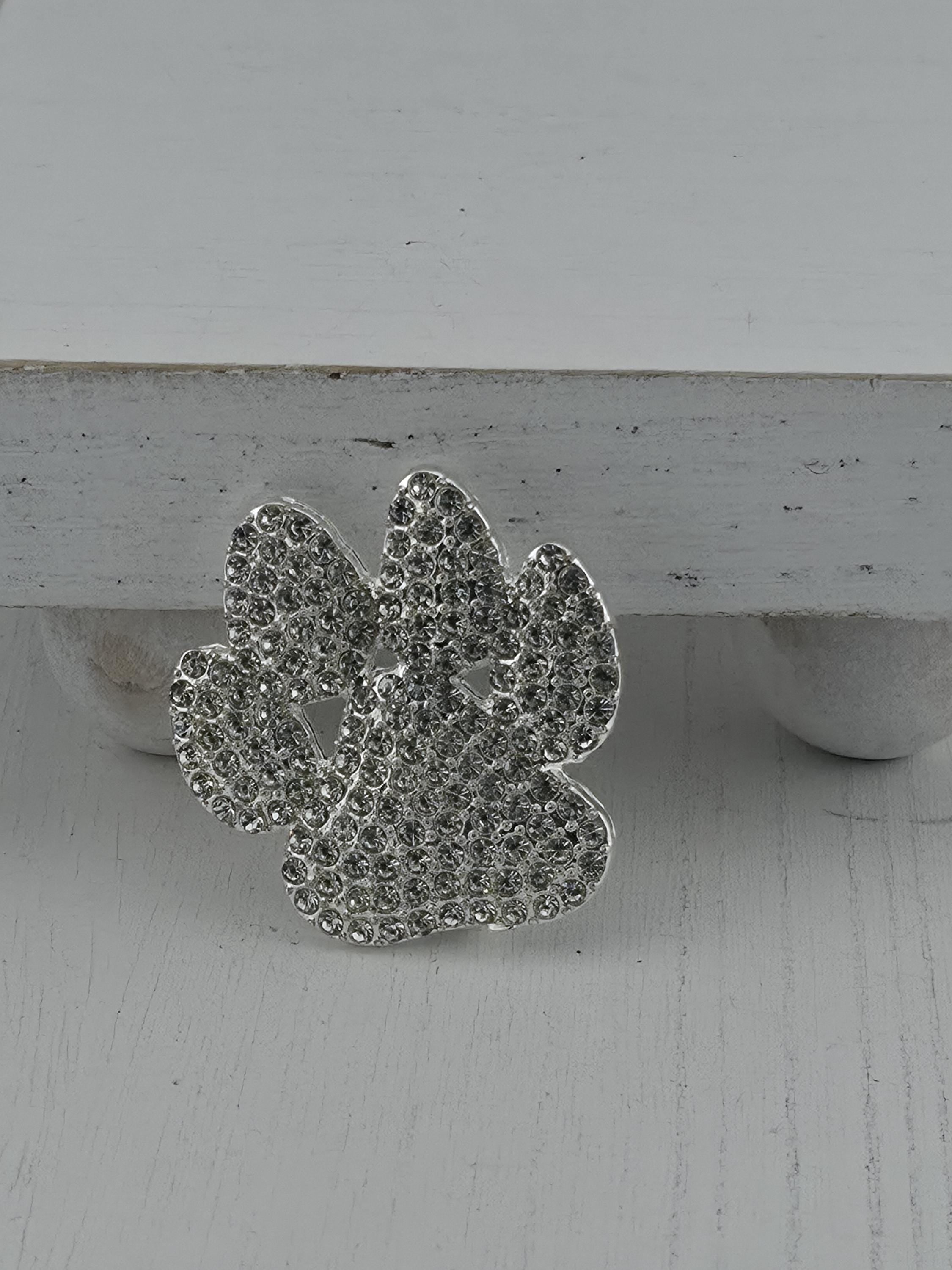 A silver, diamond-encrusted piece of jewelry is displayed against a white wooden background.