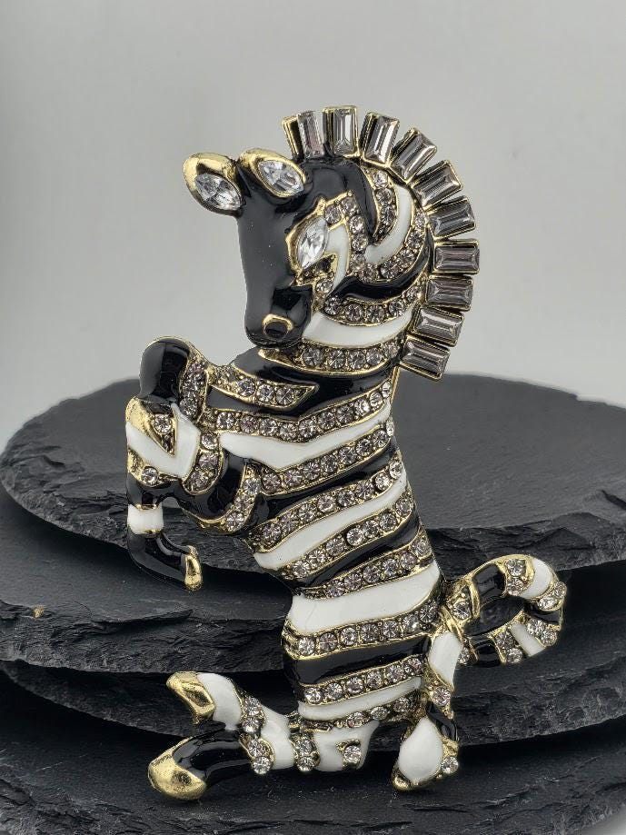 A decorative zebra brooch with a black and white striped pattern, adorned with rhinestones and a large rhinestone on its head.