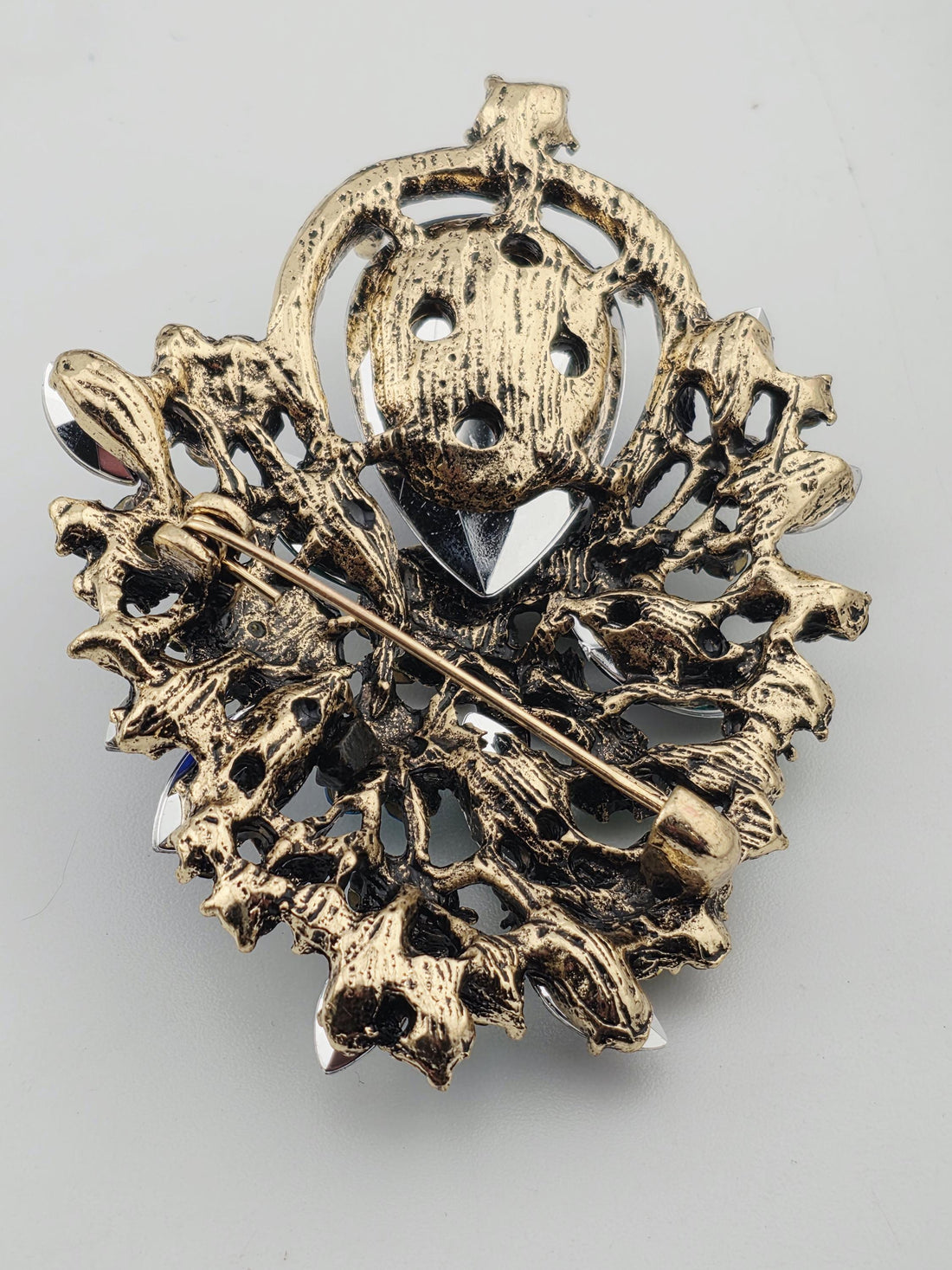 A decorative brooch with a variety of colorful gemstones, including blue, green, pink, and white stones, set within an ornate frame.