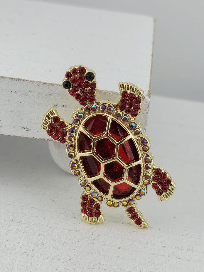 A decorative red and gold turtle brooch with rhinestones on its shell and legs.