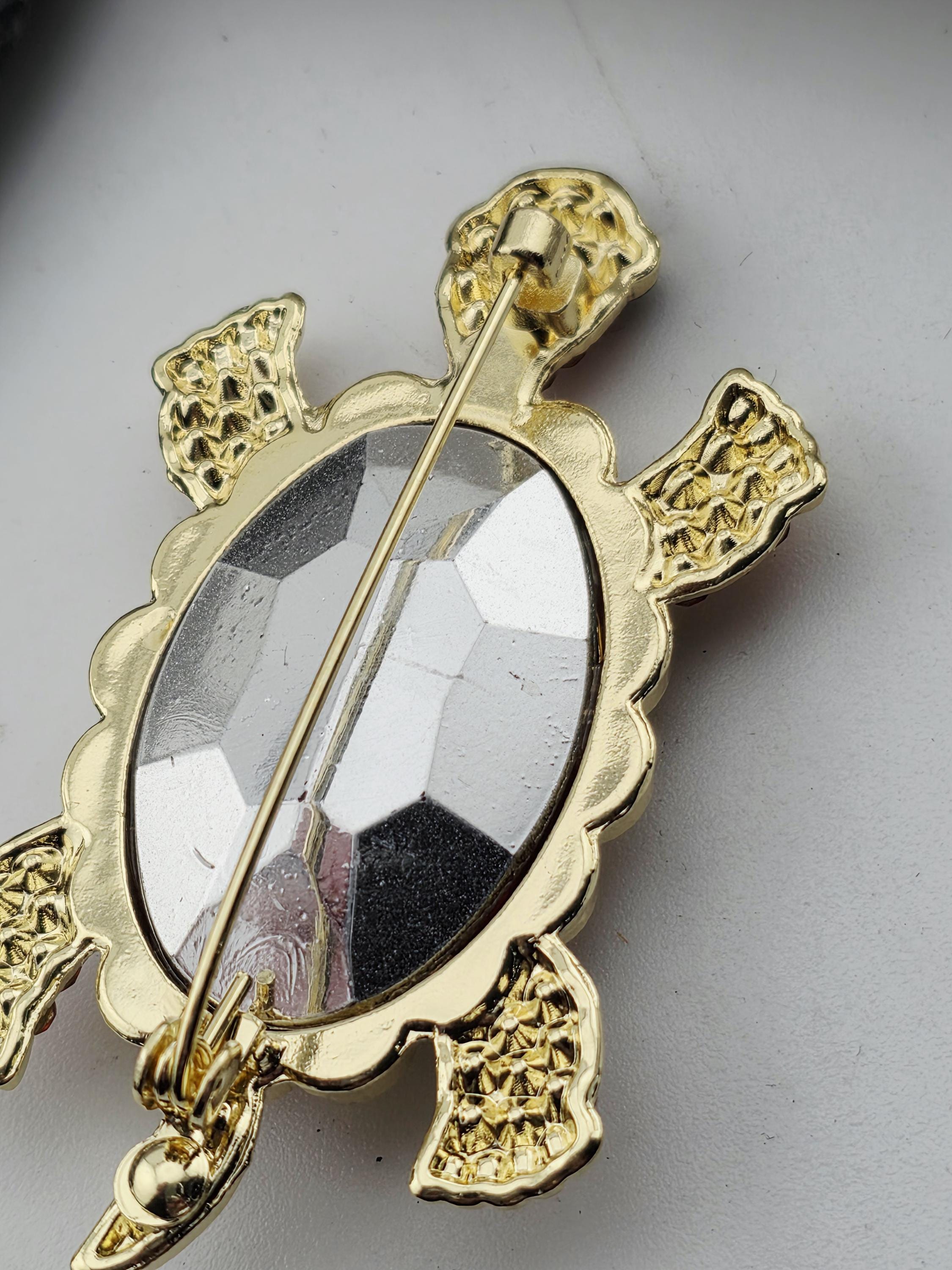A decorative gold-colored pin or brooch in the shape of a turtle, with a clear gemstone or crystal in the center.