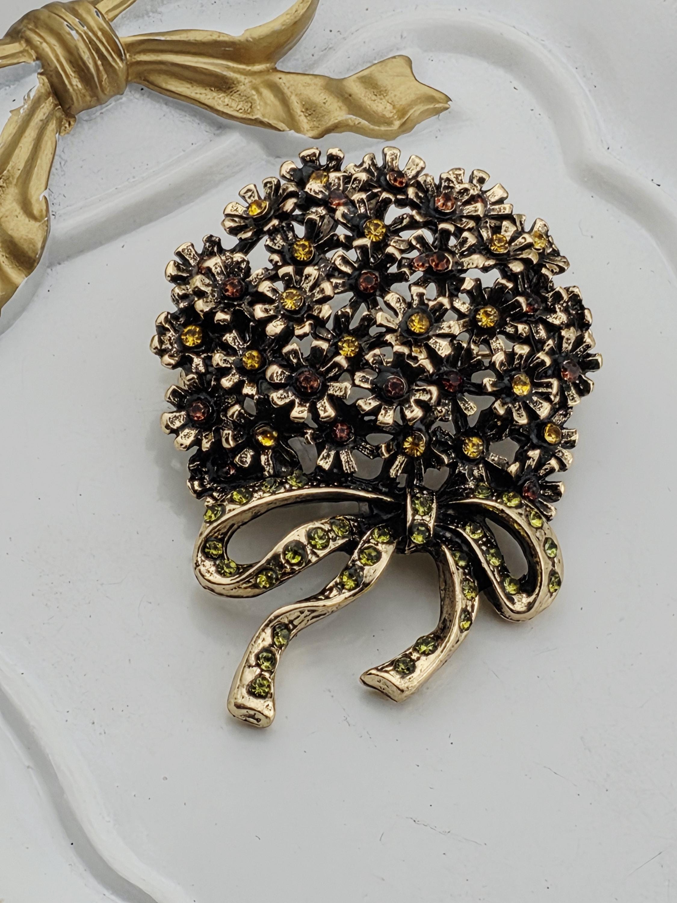 A decorative brooch with a floral design and a ribbon-like element, featuring a mix of gold and green gemstones.
