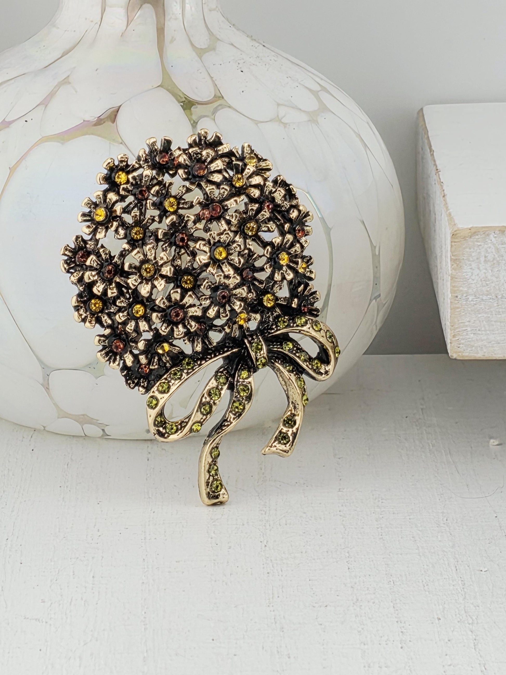 A decorative brooch with a floral design and a ribbon-like element is displayed on a white surface.