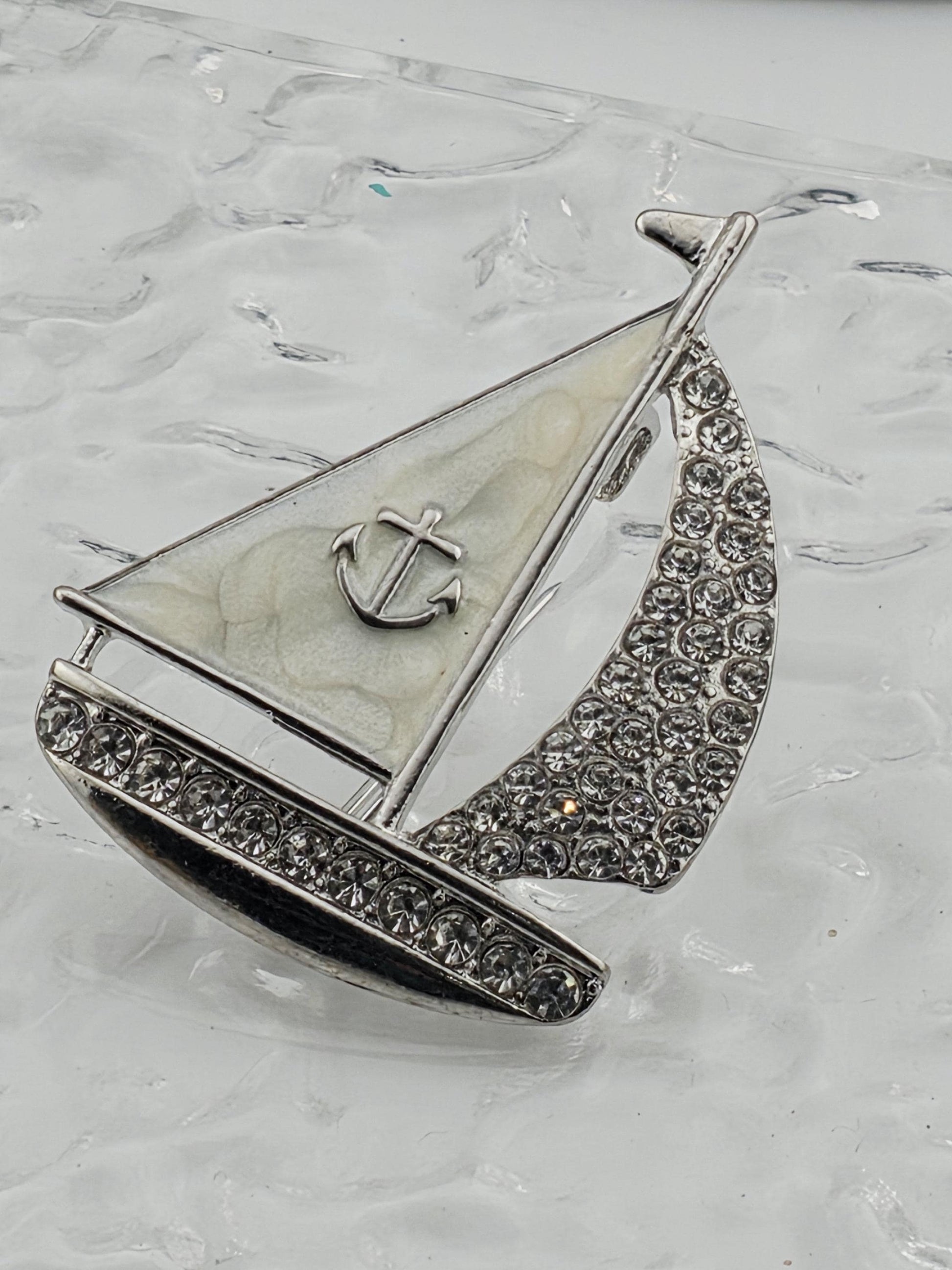 A silver-colored brooch with a boat-shaped design and a small anchor symbol, set against a white background.