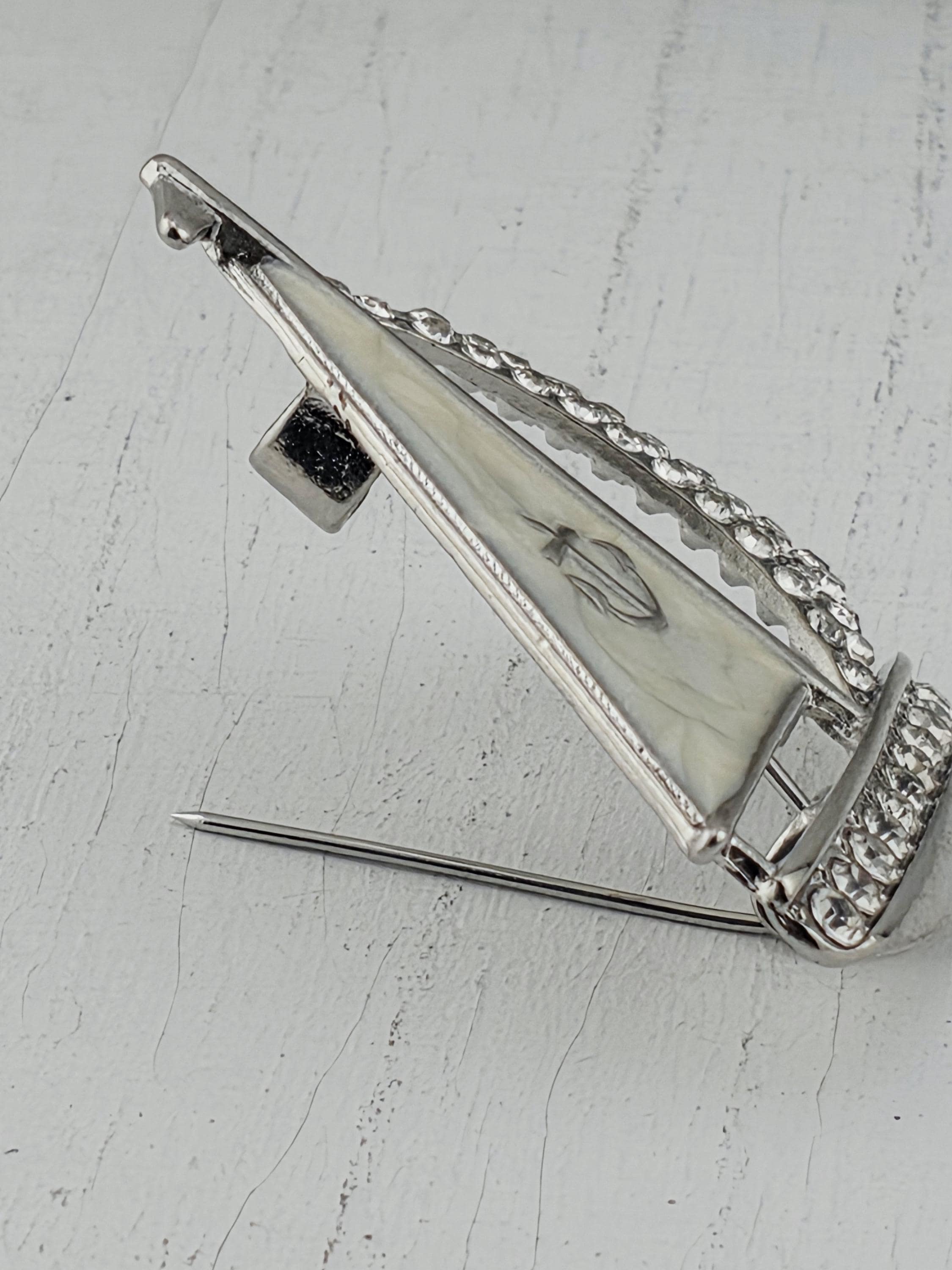 A silver pin with a diamond-encrusted design, attached to a white wooden surface.