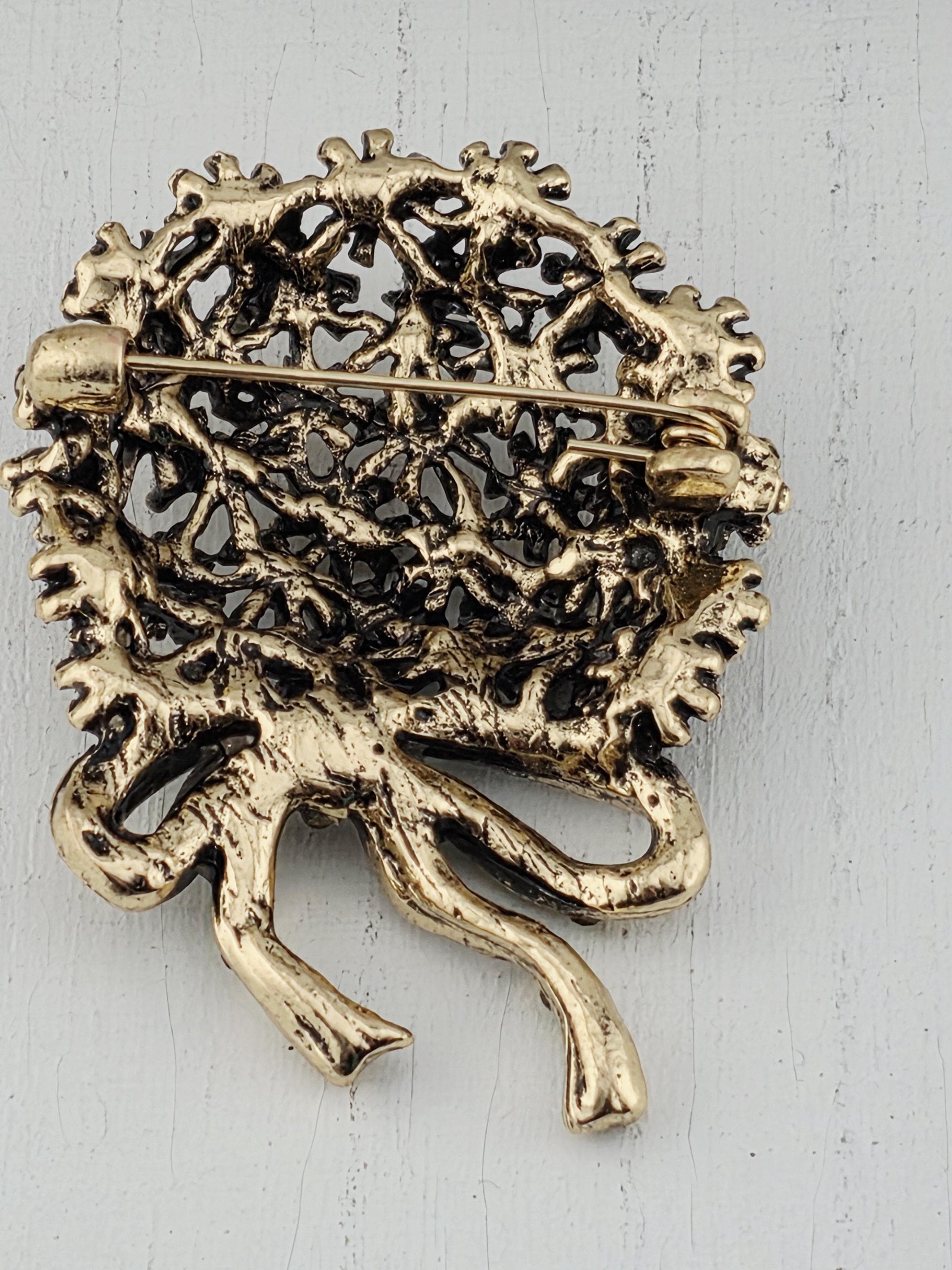 A decorative gold-colored pin or brooch with an intricate, textured design.