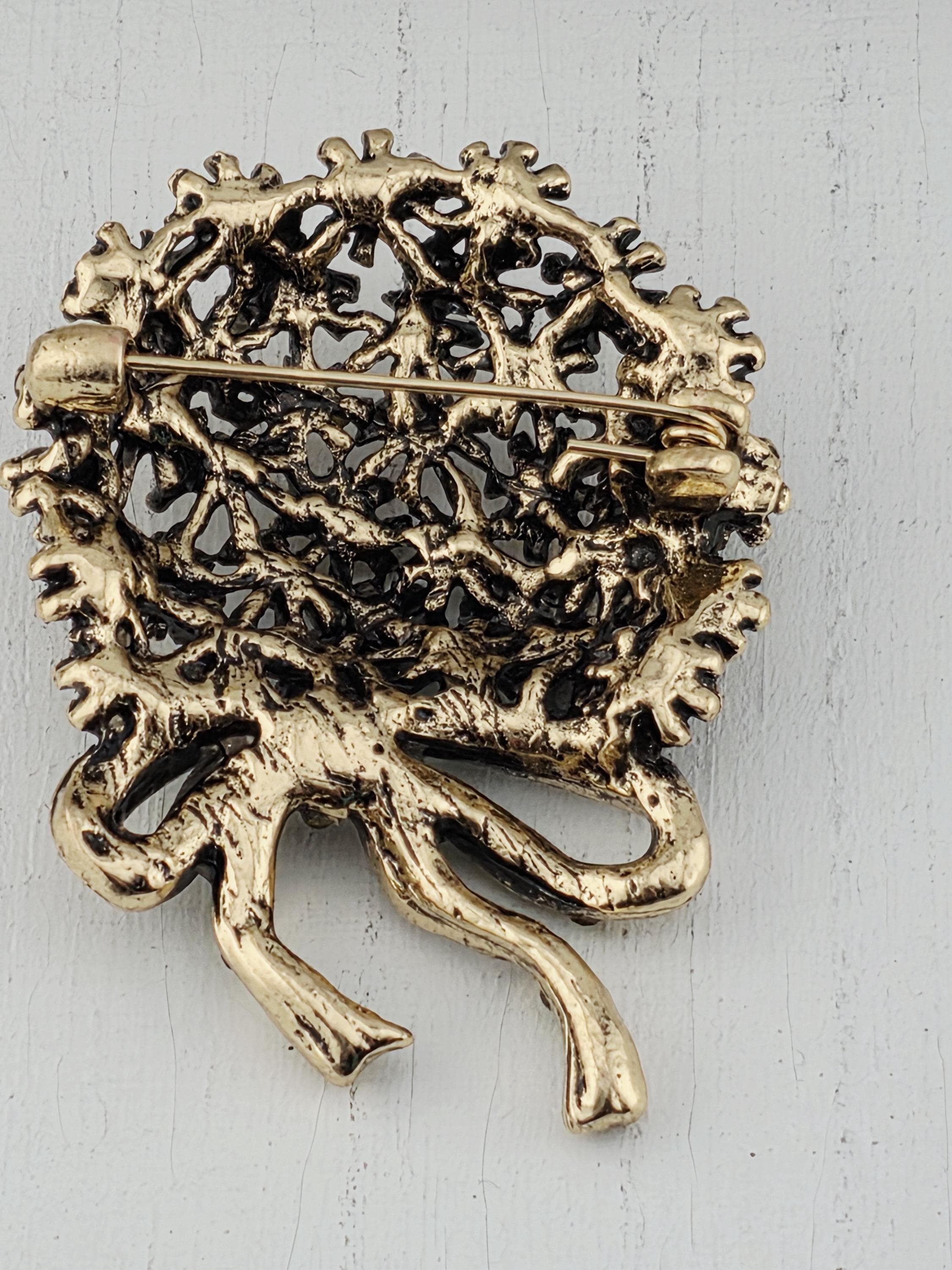 A decorative gold-colored pin or brooch with an intricate, textured design.
