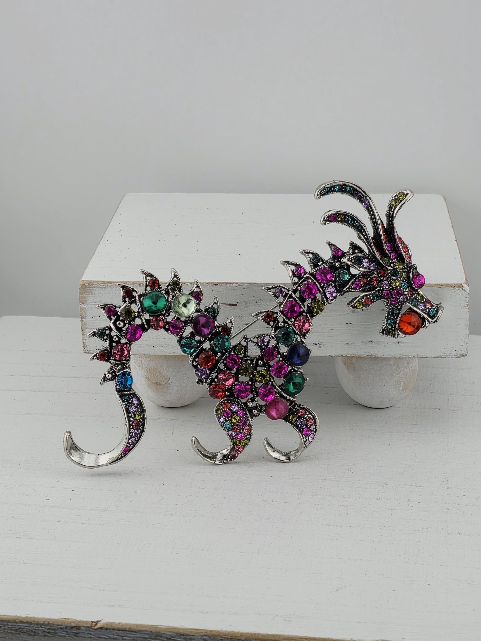 A colorful, ornate dragon-shaped brooch or pendant adorned with various gemstones and metallic elements.