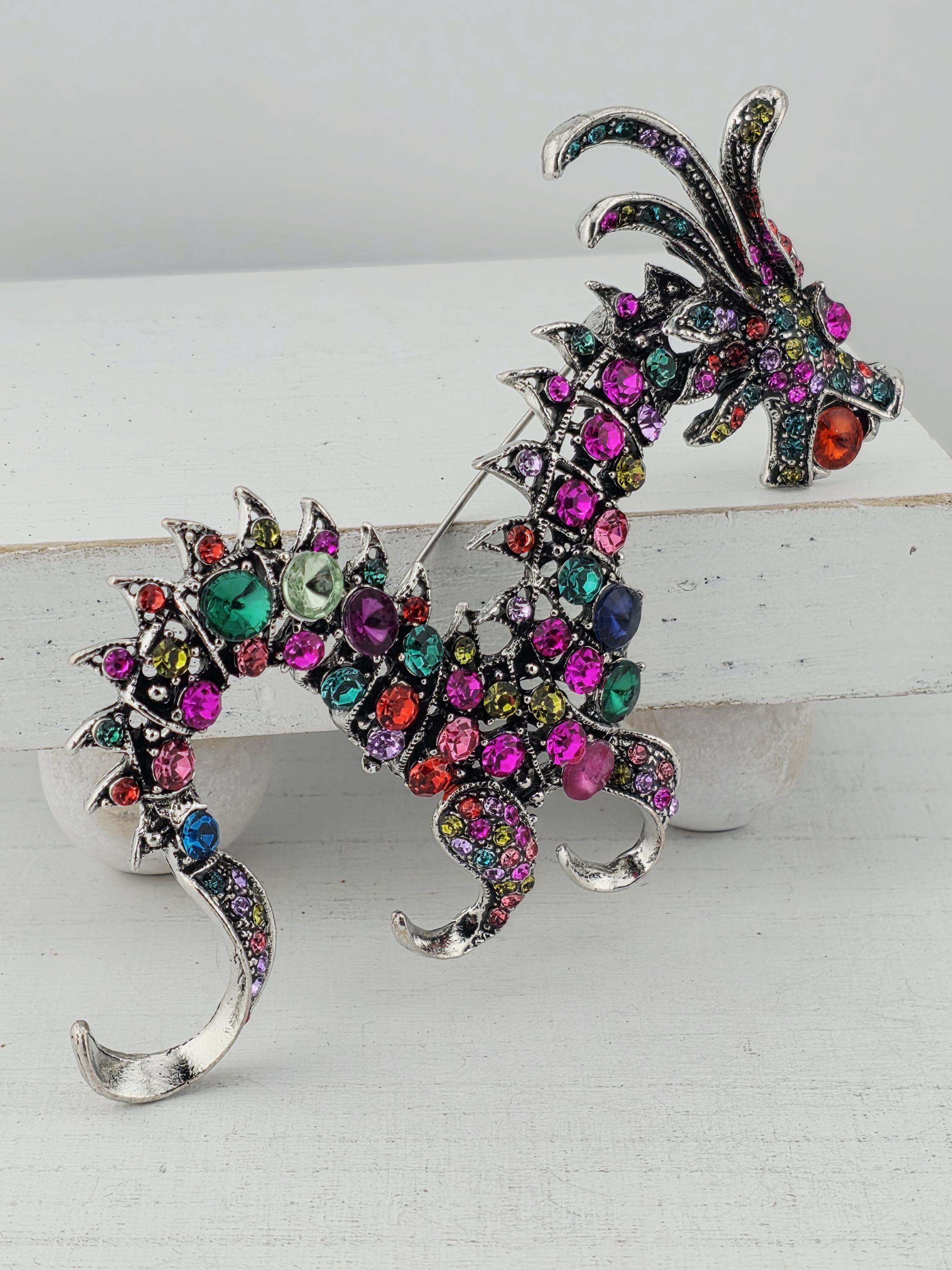 A colorful, sparkling dragon brooch with a variety of gemstones and metallic elements.