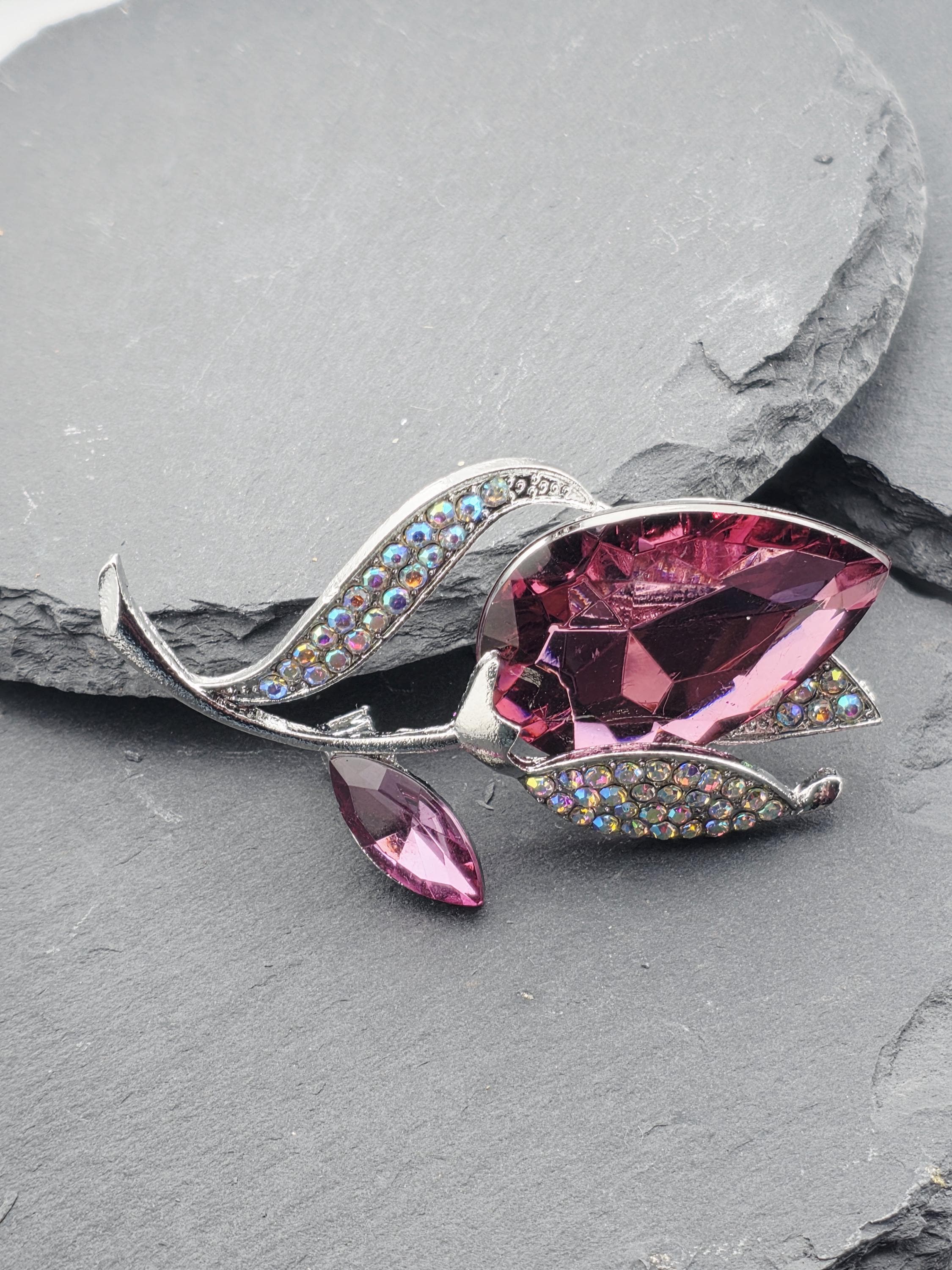 A pink crystal brooch with a floral design and rhinestones is displayed on a gray surface.