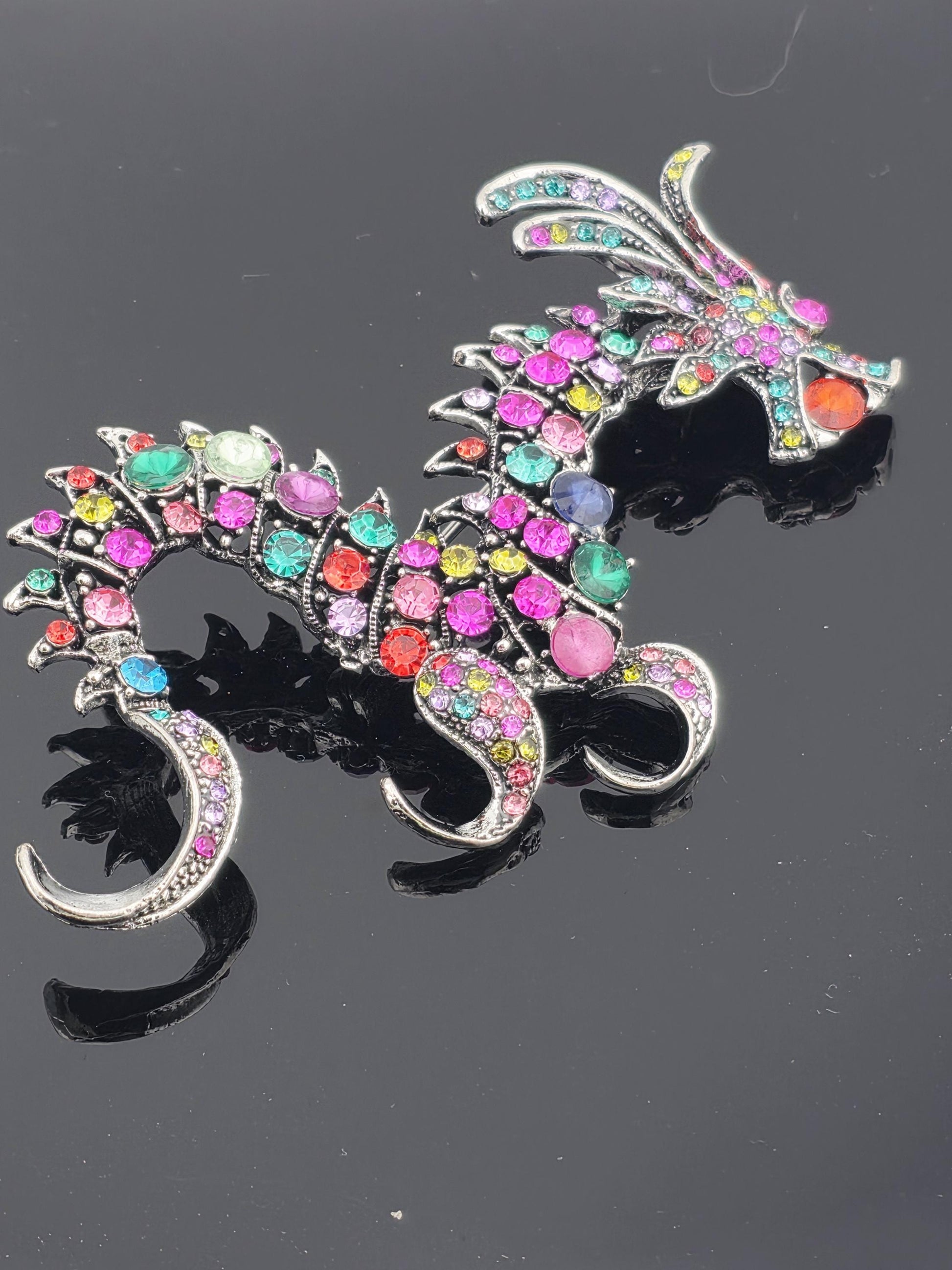 A colorful, ornate brooch or pendant with a dragon-like design, featuring a variety of gemstones and metallic elements.
