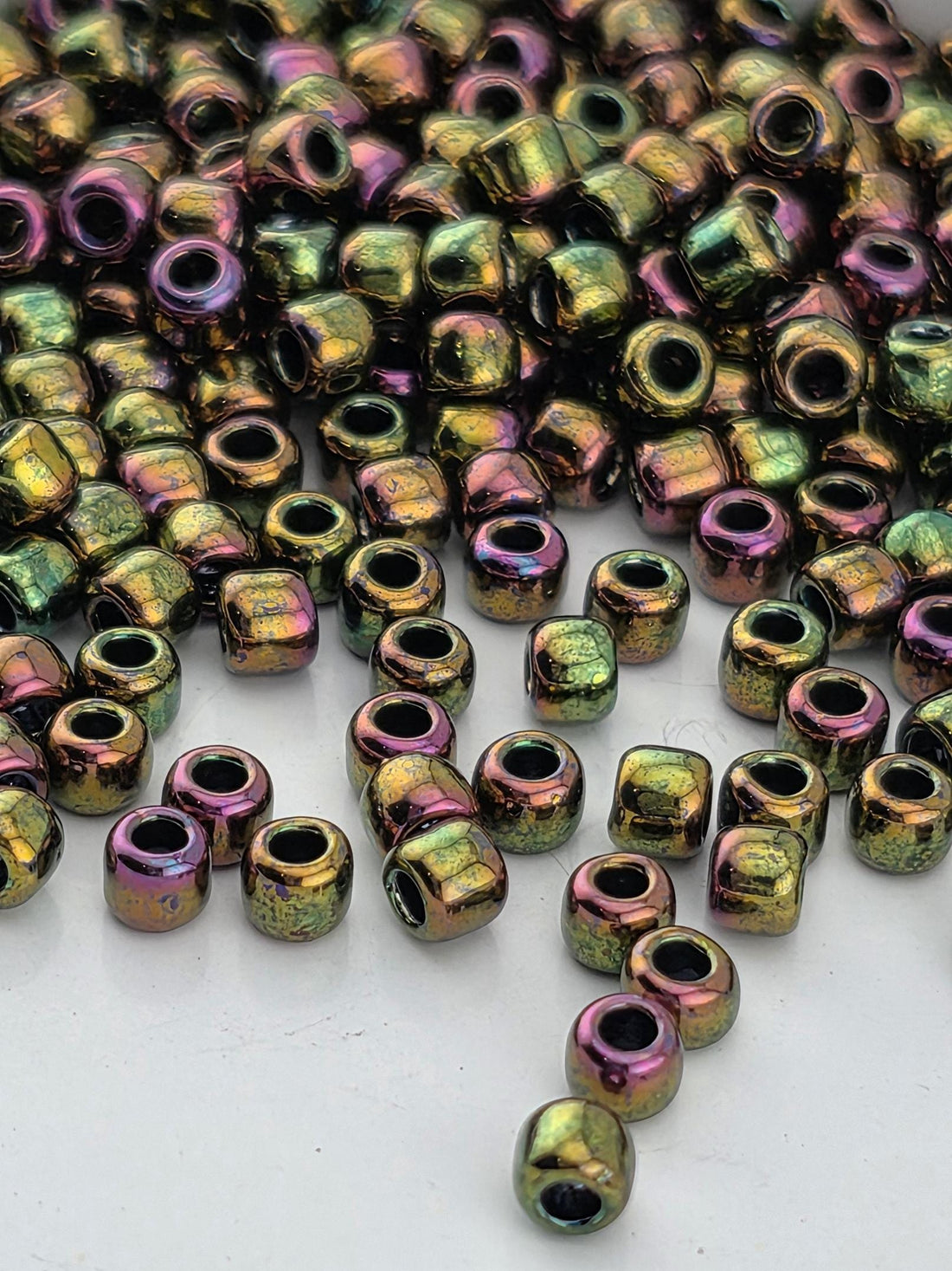 a close-up view of a pile of multicolored beads, including green, purple, and gold-colored beads, scattered on a white surface.