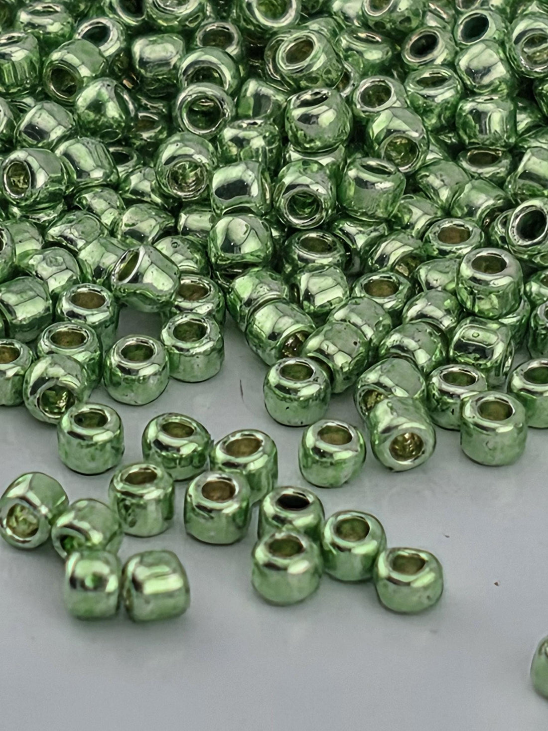a close-up view of numerous small, shiny green beads or beads scattered on a surface.
