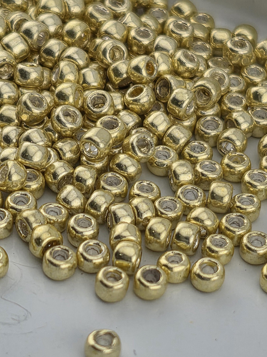A close-up image of numerous small, shiny gold beads or beads arranged in a pile.
