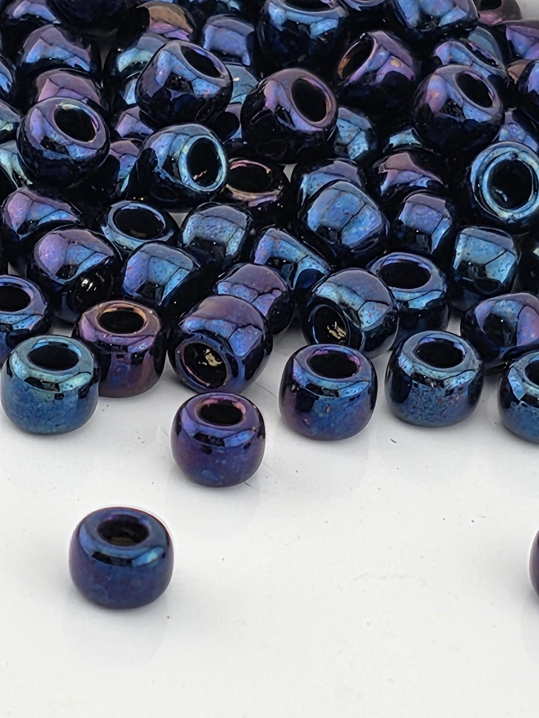 a collection of multicolored glass beads, including blue, purple, and black, scattered on a white surface.