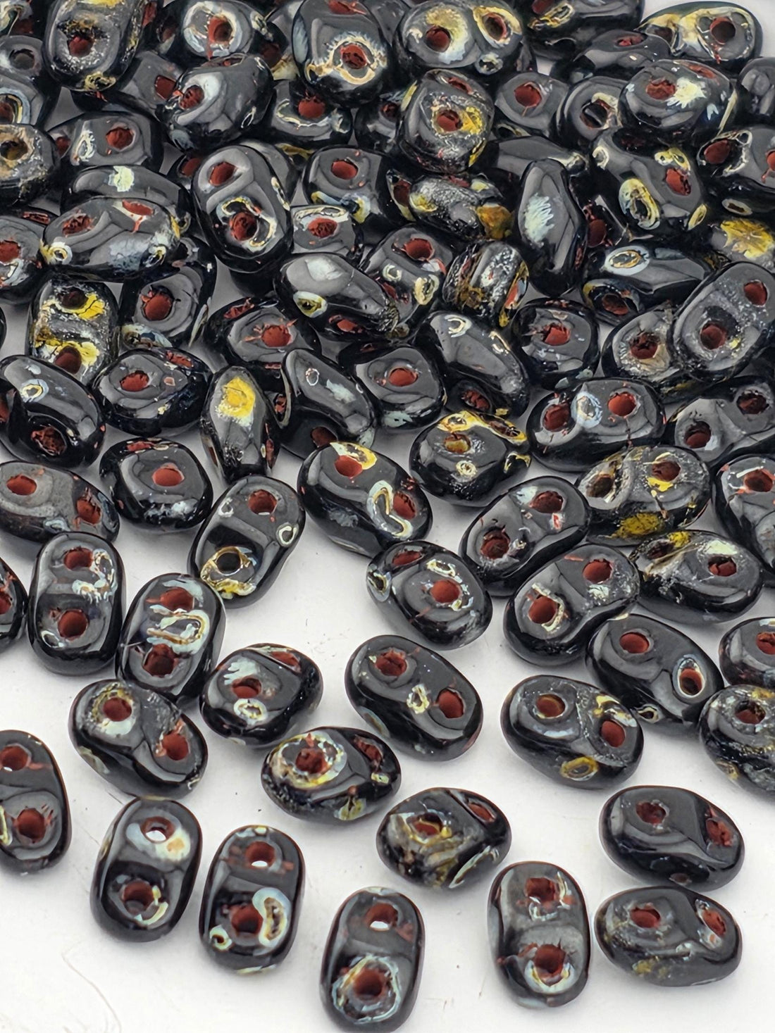 a collection of black beads with red and yellow accents, scattered across a white surface.