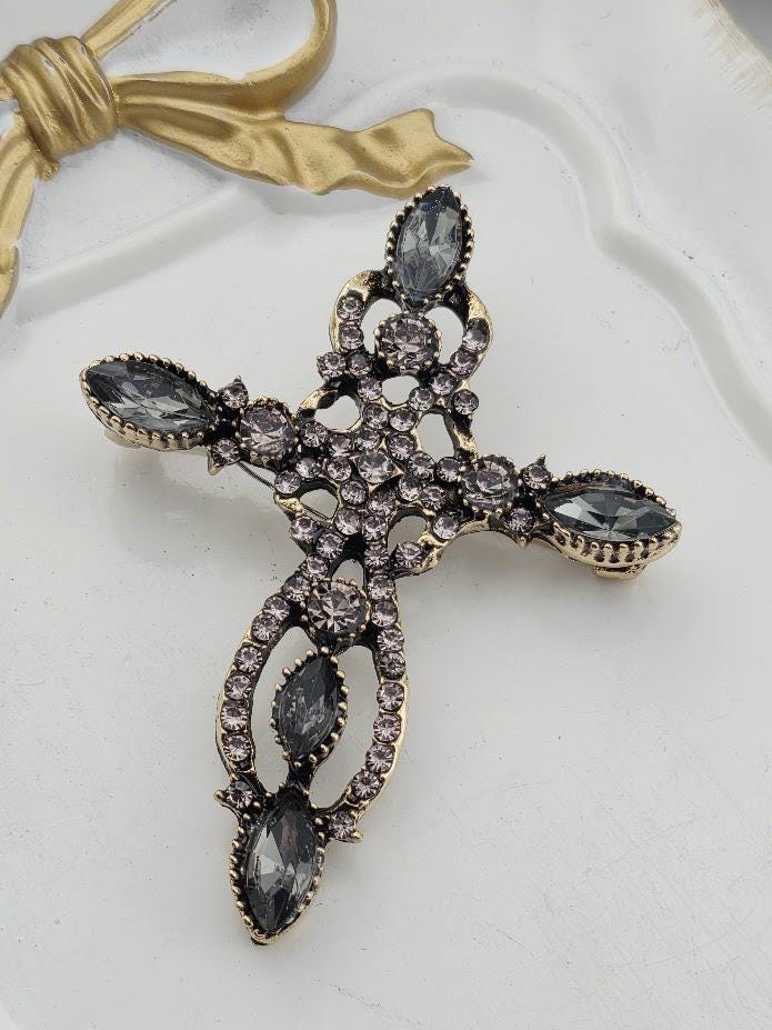 A decorative cross-shaped brooch with a gold-colored frame and sparkling crystal stones.