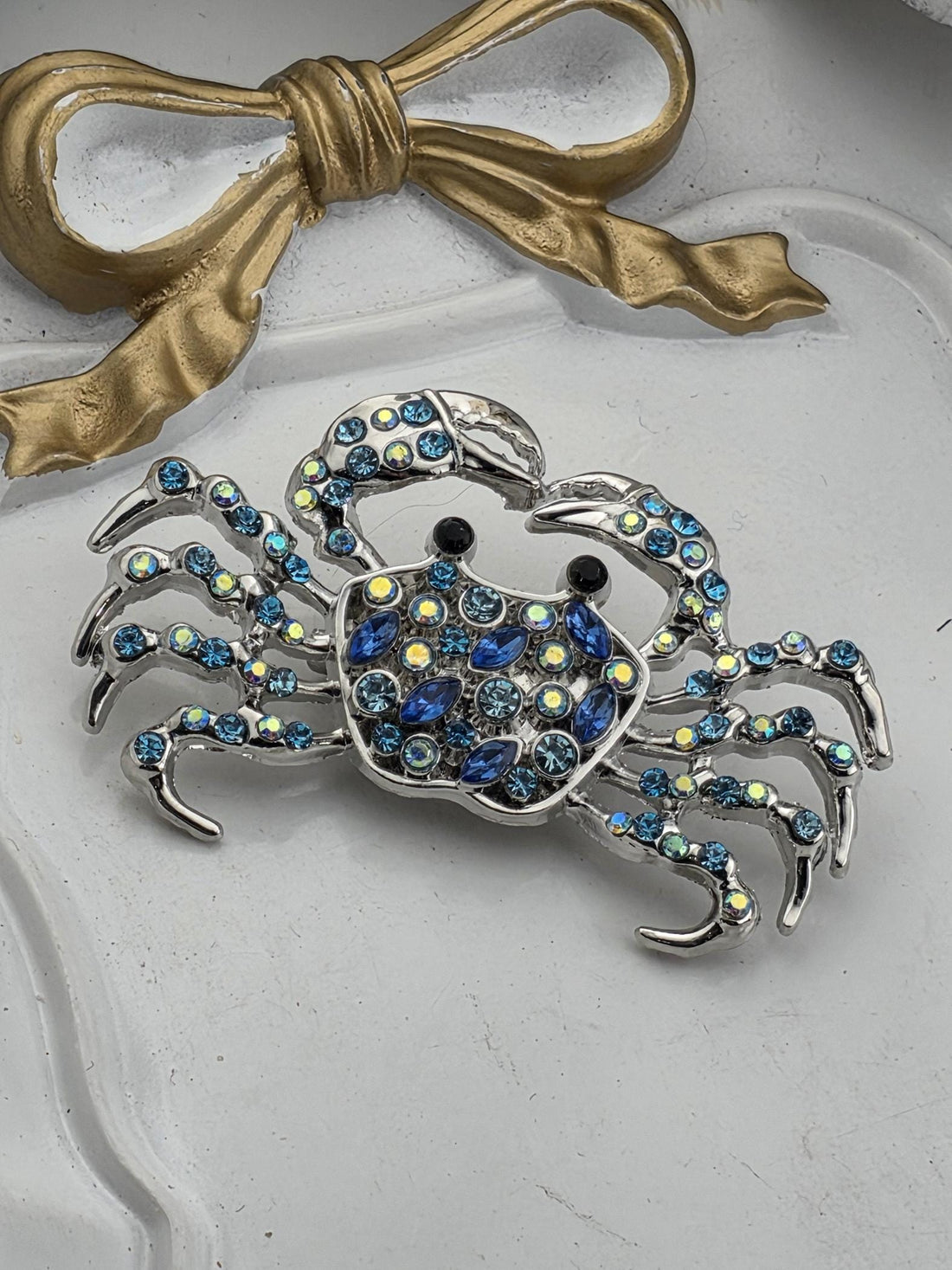 a close-up view of a decorative crab-shaped piece of jewelry, adorned with numerous blue gemstones. The crab is intricately designed and appears to be the focal point of the image.