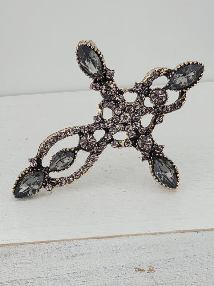A decorative cross-shaped piece of jewelry with a combination of black and silver elements, including gemstones.