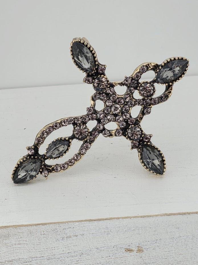 A decorative cross-shaped piece of jewelry with a combination of black and silver elements, including gemstones.
