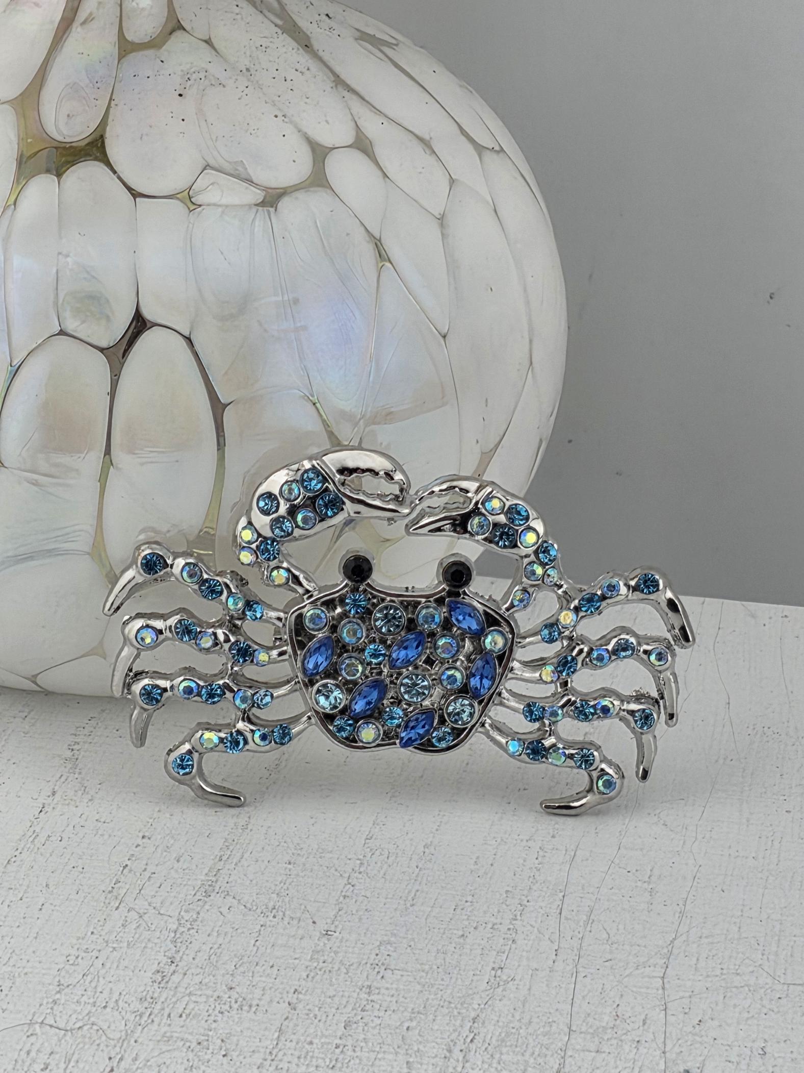 A silver crab brooch adorned with blue gemstones is displayed against a white background.