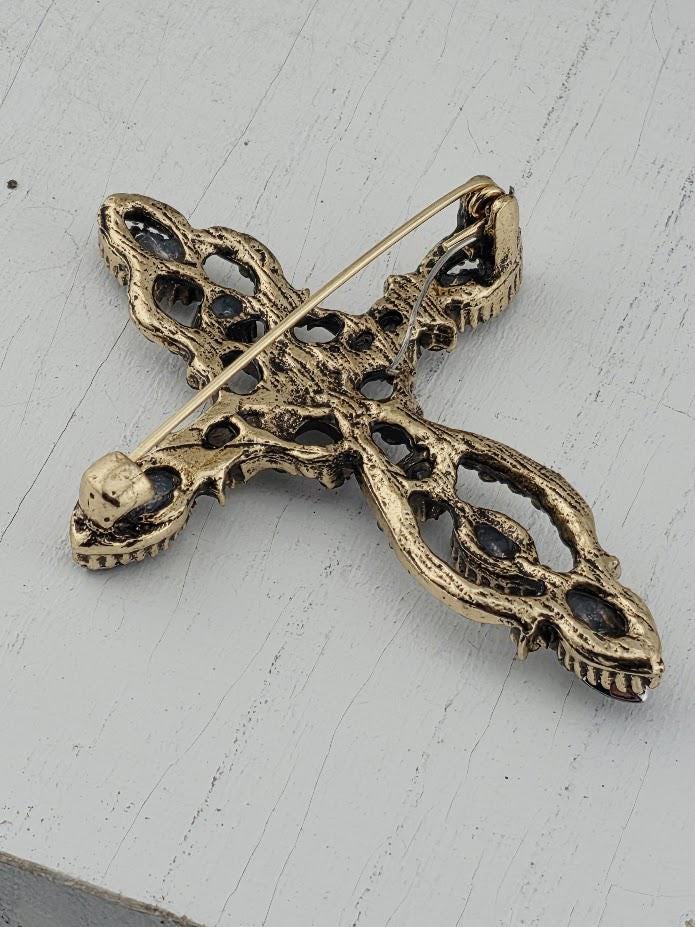 A decorative cross-shaped brooch with intricate patterns and designs, resting on a white surface.