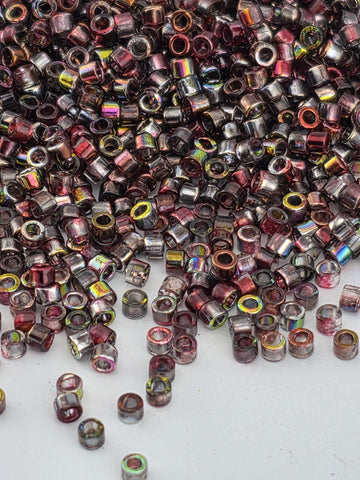 a large pile of multicolored beads, including various shades of red, purple, and yellow, scattered across a white surface.