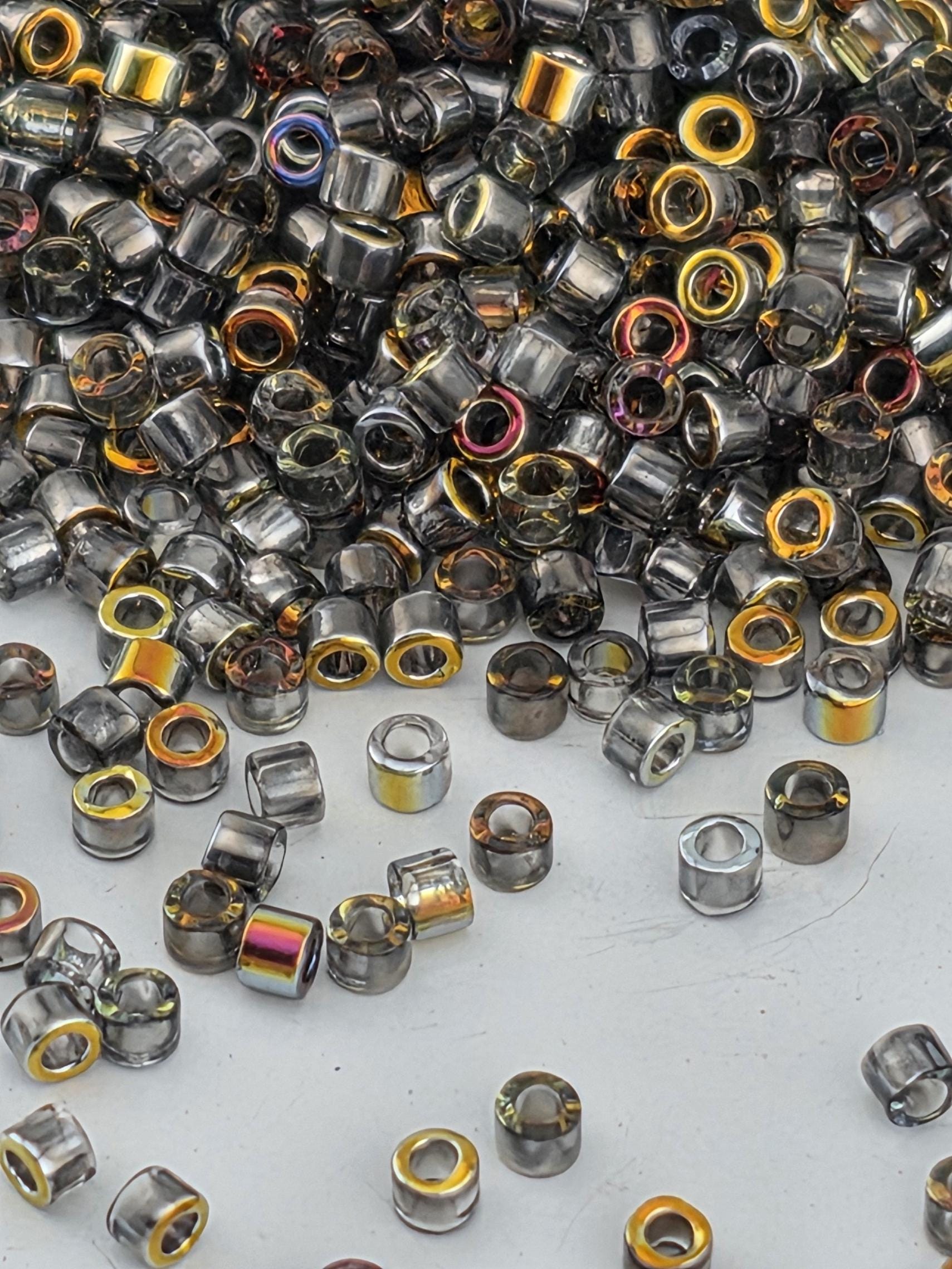 a large pile of various colored glass beads, including silver, gold, and multicolored glass pieces, scattered across a white surface.