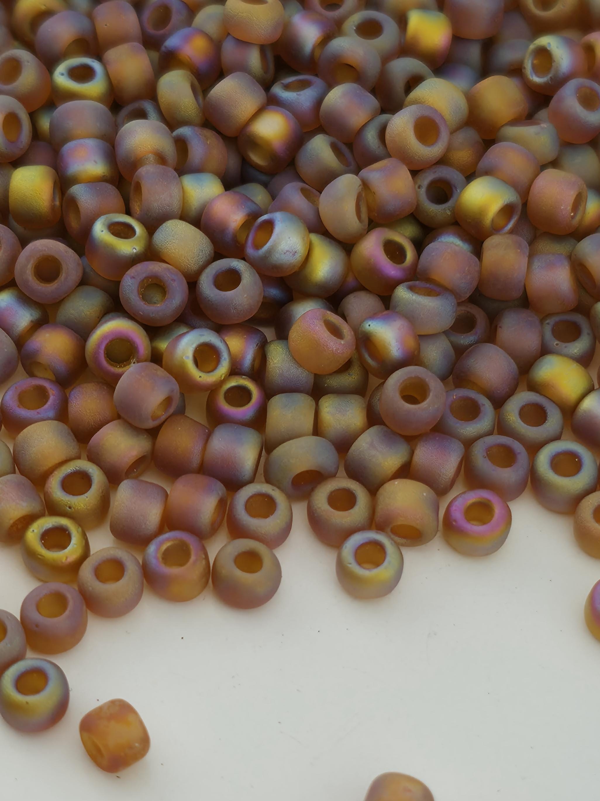 A close-up image of a pile of multicolored beads, including various shades of orange, yellow, and purple, scattered on a white surface.