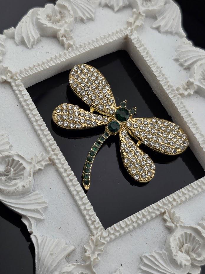 A decorative white frame with a gold-colored brooch featuring a diamond-encrusted dragonfly design.