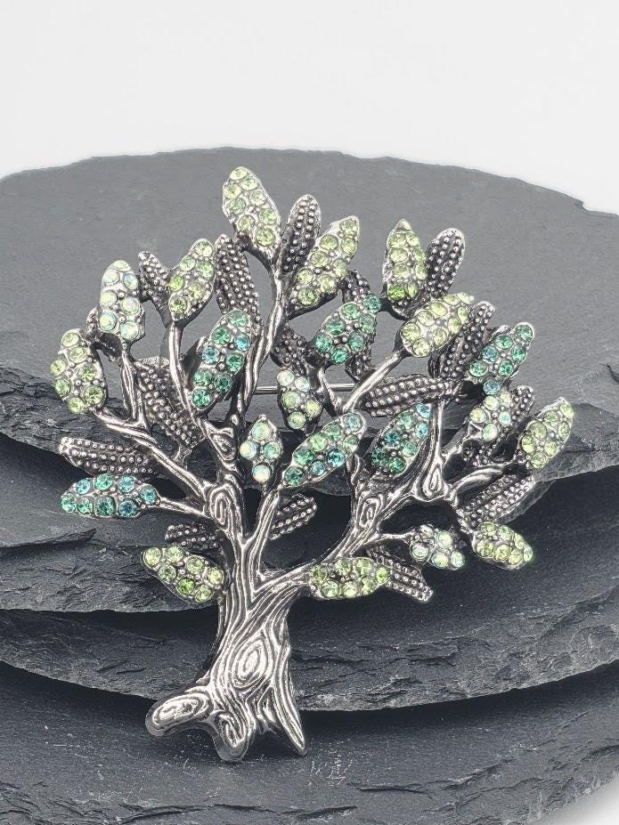 A decorative brooch in the shape of a tree, adorned with green and blue gemstones.