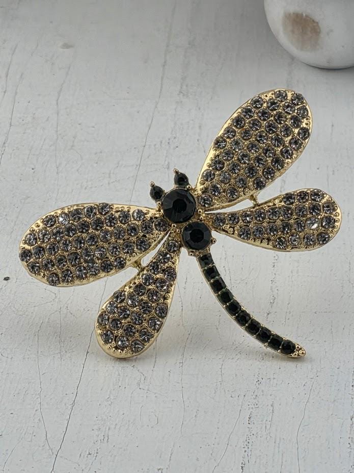A decorative piece featuring a gold-colored dragonfly with black gemstones on its wings and a black tail.