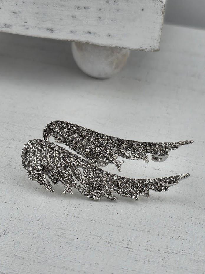 A pair of silver-colored wing-shaped earrings with sparkling rhinestones or crystals on a white surface.