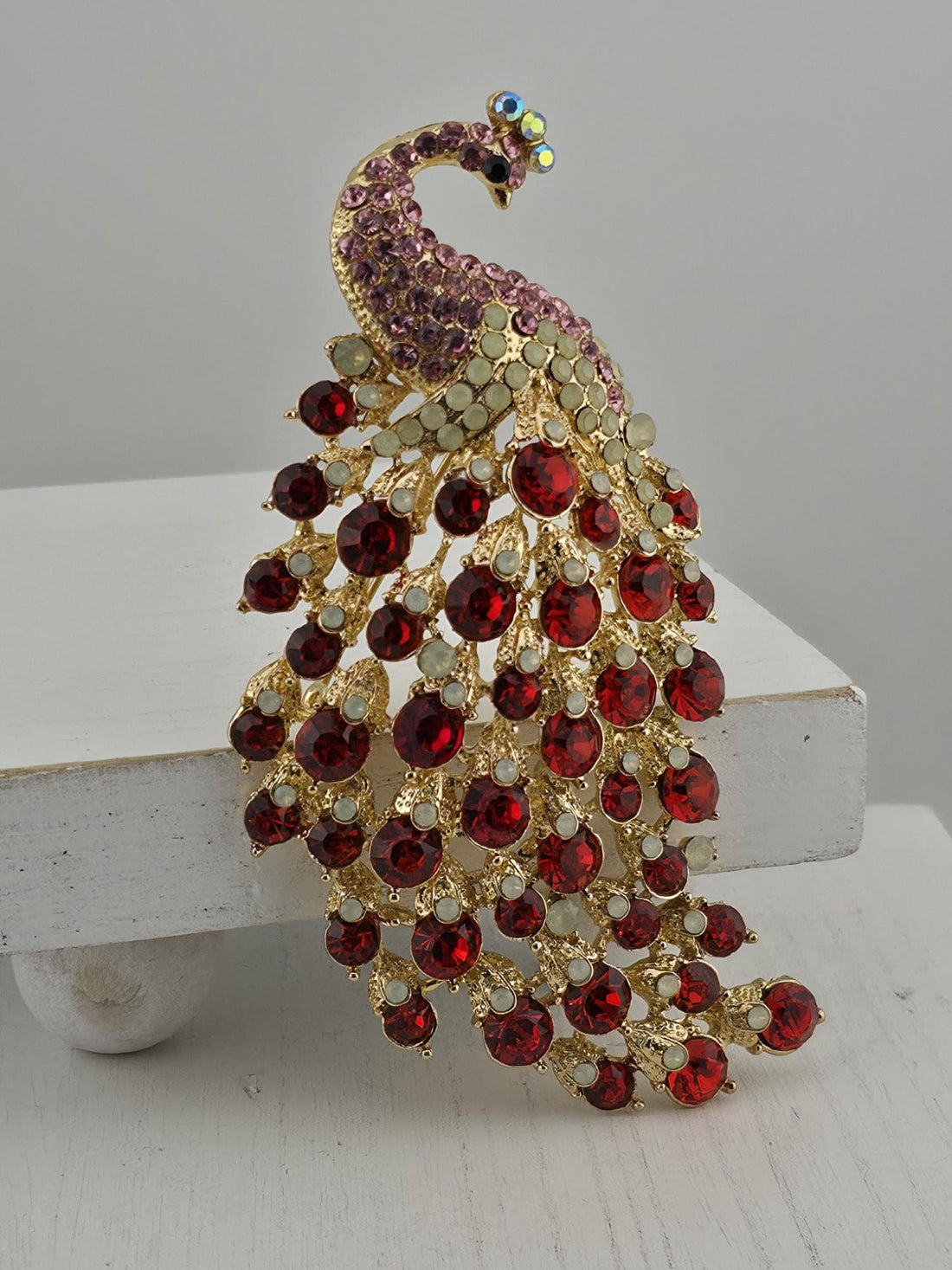 A decorative brooch in the shape of a peacock, adorned with red and gold gemstones.