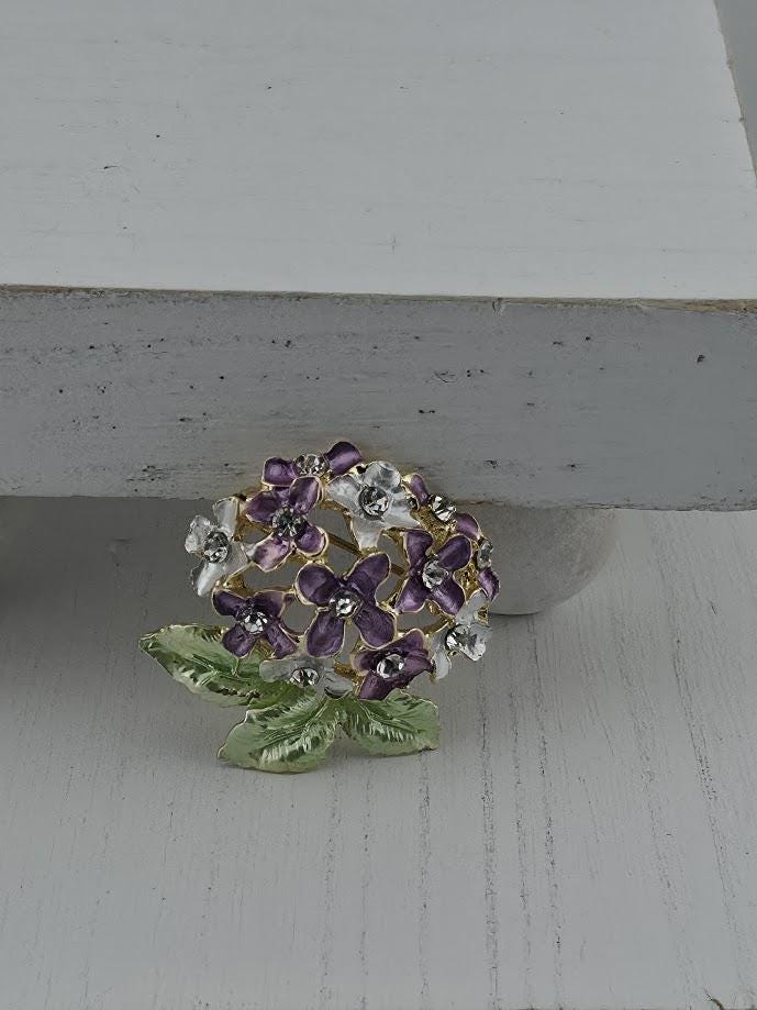 A decorative brooch with a floral design and sparkling gemstones is displayed on a white surface.