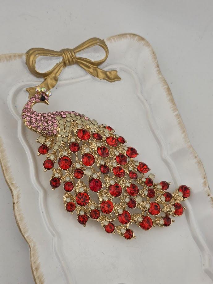 A decorative peacock brooch with a gold bow and a large arrangement of red gemstones.