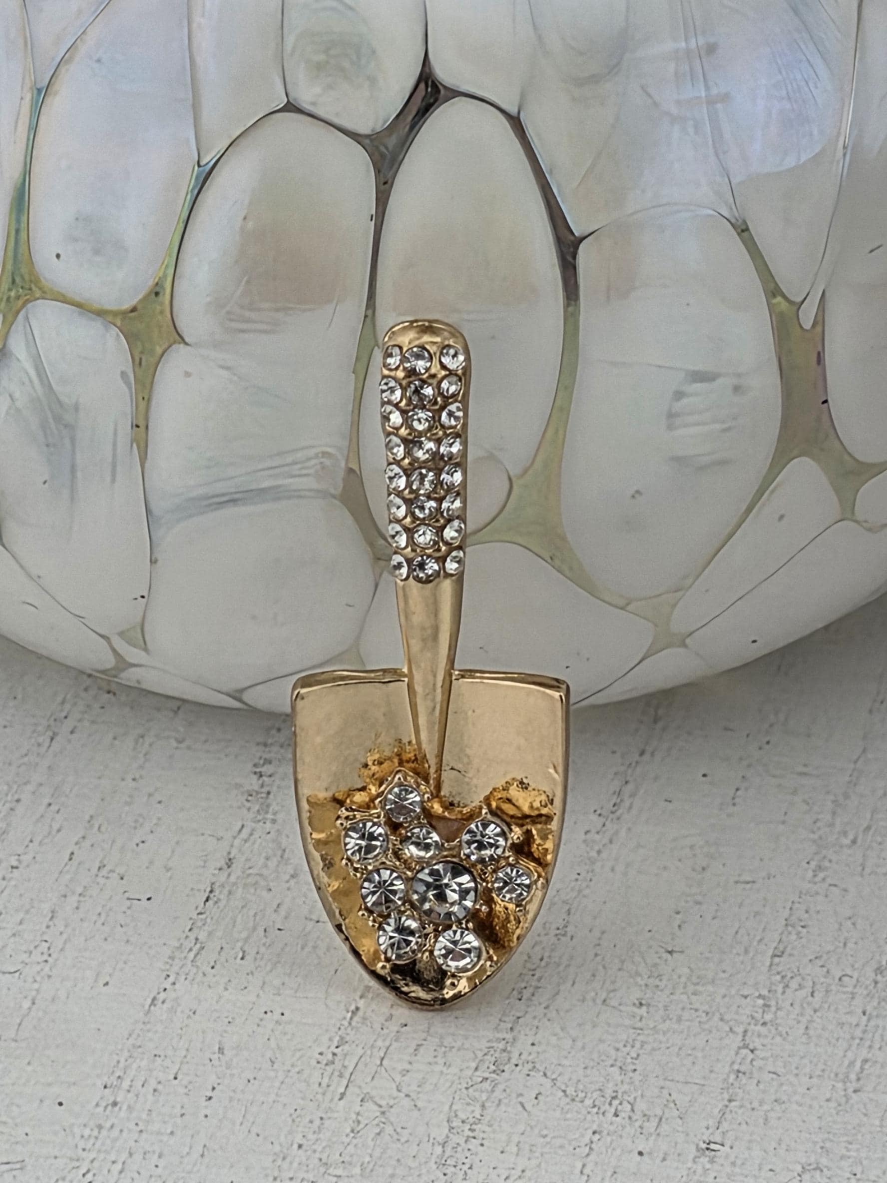 A close-up view of a gold-colored brooch with a diamond-encrusted handle, placed on a white surface.