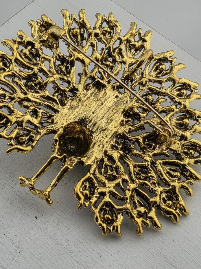 a decorative golden brooch with an intricate, organic design.