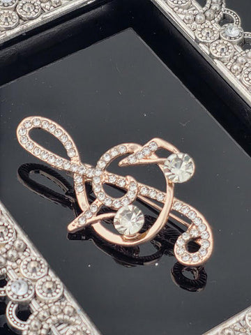 A close-up image of a decorative piece featuring a musical note motif, with a shiny gold-colored design and sparkling rhinestones or crystals.